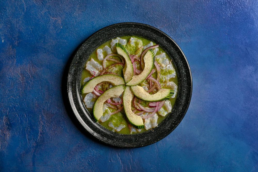 Aguachile verde en plato negro con aguacate y cebolla